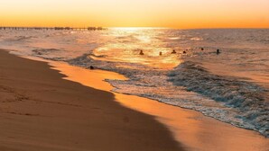 A beach with a pier extending into the ocean during sunset.