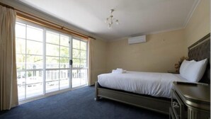 Una habitación de hotel con un ventanal grande, una cama, una mesita de noche y un ventilador de techo.