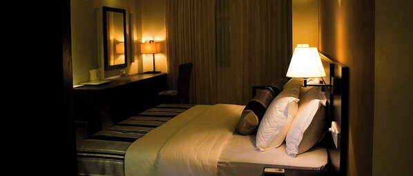 Une chambre d’hôtel avec un lit, des lampes de chevet, un bureau et un miroir.