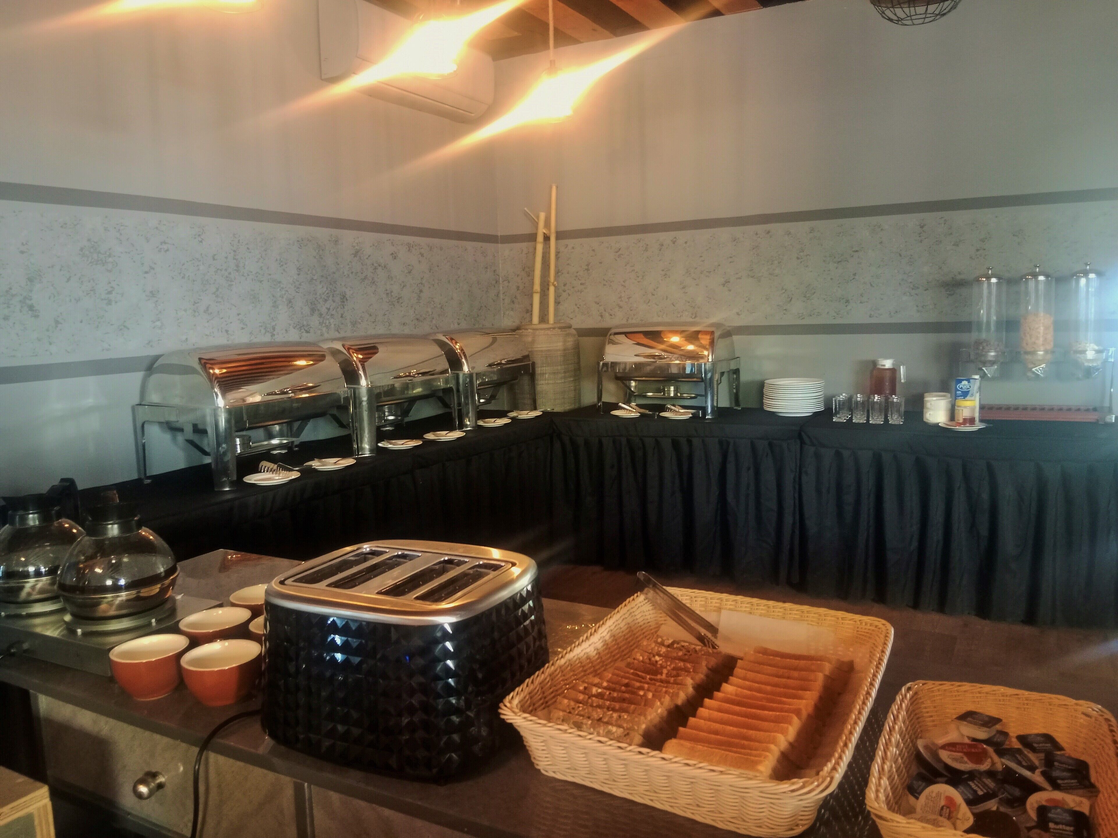 Un buffet avec différents postes de service proposant une variété de plats, notamment un grille-pain, des paniers à pain et un distributeur de boissons.