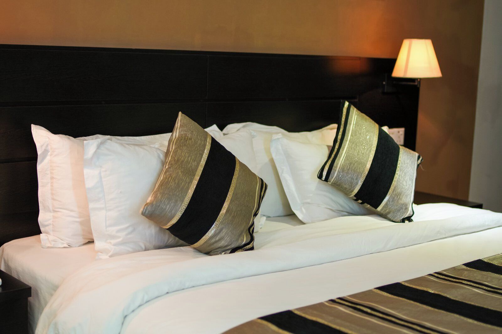 A neatly made bed with white and striped pillows, a black headboard, and a lamp on the side.