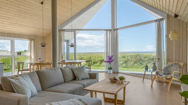 A spacious room with a large window, a wooden ceiling, a sofa, a table, and a chair. - "Tilje" - 80m from the sea by Interhome (Hjørring)