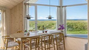 A dining area with a large table and chairs, large windows with a view of the sea, and hanging pendant lights. - "Tilje" - 80m from the sea by Interhome (Hjørring)