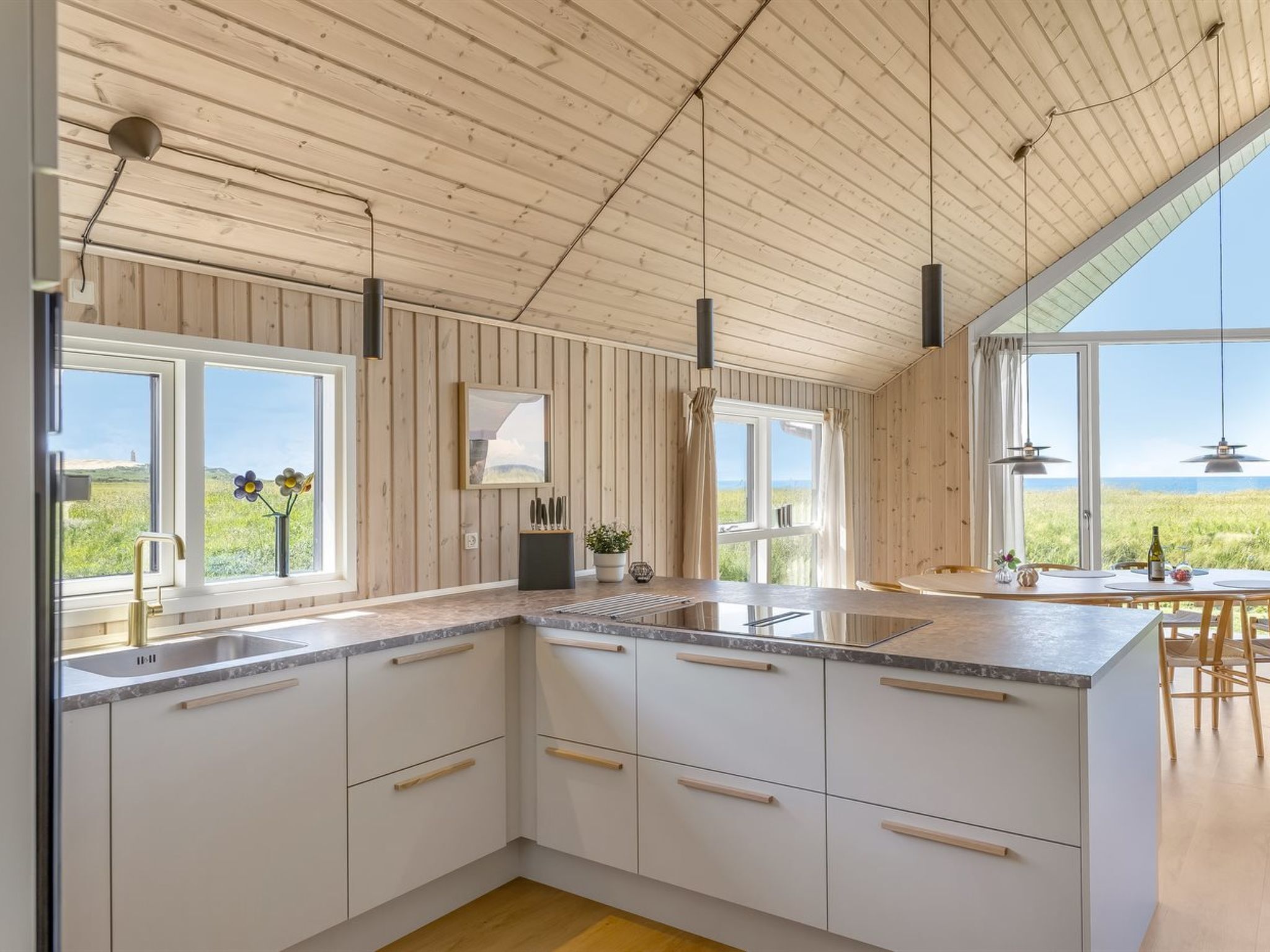 Et moderne køkken med træpaneler, store vinduer og udsigt til naturen.