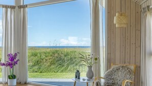 A room with large windows, a wooden chair, a small table, and a vase with flowers. - "Tilje" - 80m from the sea by Interhome (Hjørring)