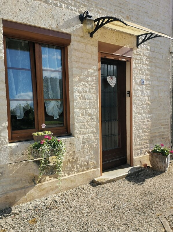 A stone building with a wooden door, a window with lace curtains, and a heart-shaped decoration on the door.