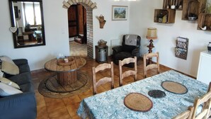 Una sala de estar rústica con una mesa de madera, sillas, un sofá y una mesa de comedor con mantel estampado.