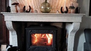 Una chimenea de piedra con estufa de leña en la parte inferior, un fuste con velas, un jarrón decorativo y un pequeño árbol de Navidad.