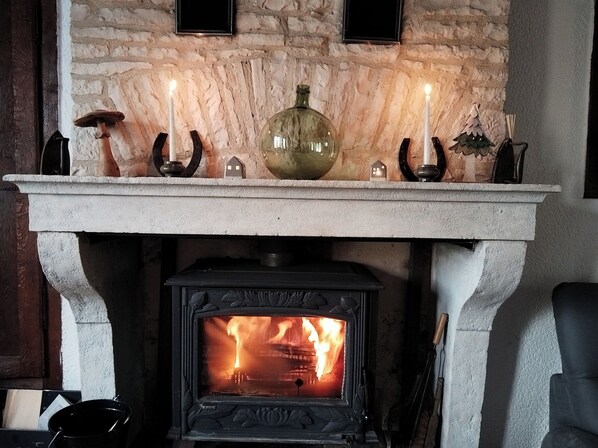 A stone fireplace with a wood-burning stove below, a mantel with candles, a decorative vase, and a small Christmas tree.