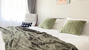 A hotel room with a bed, a green blanket, white pillows, and a window with curtains. - Charming 3-bedroom house with AC, WiFi in marvelous Bangkok (Krung Thep Maha Nakhon)