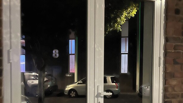 A white-framed window with two panes, reflecting a street scene with parked cars and a building with a visible number '8'. - 2 Double 3 Single  2 Sofa Beds Studio (Auckland)