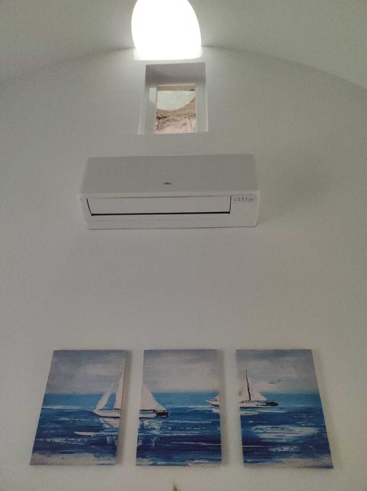 Une pièce dotée d’un climatiseur fixé au mur, d’une petite fenêtre située au-dessus et de trois tableaux représentant des voiliers accrochés au mur.