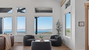 Un salon spacieux doté de grandes fenêtres offrant une vue sur la mer et les montagnes.