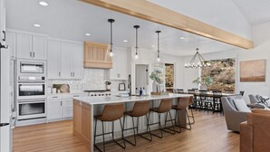 Une cuisine moderne avec des meubles blancs, un îlot central doté de tabourets de bar et un coin repas offrant une vue agréable.