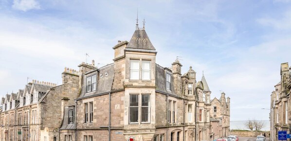 A historic stone building with a prominent corner turret, large windows, and a view of the sea.