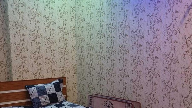 A bedroom with a wooden bed, patterned wallpaper, and a ceiling light. - Dev In Guest House (Varanasi)