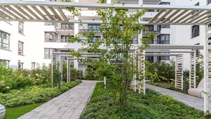 Un moderno complejo de apartamentos con un patio central, pasillos cubiertos y abundante vegetación.