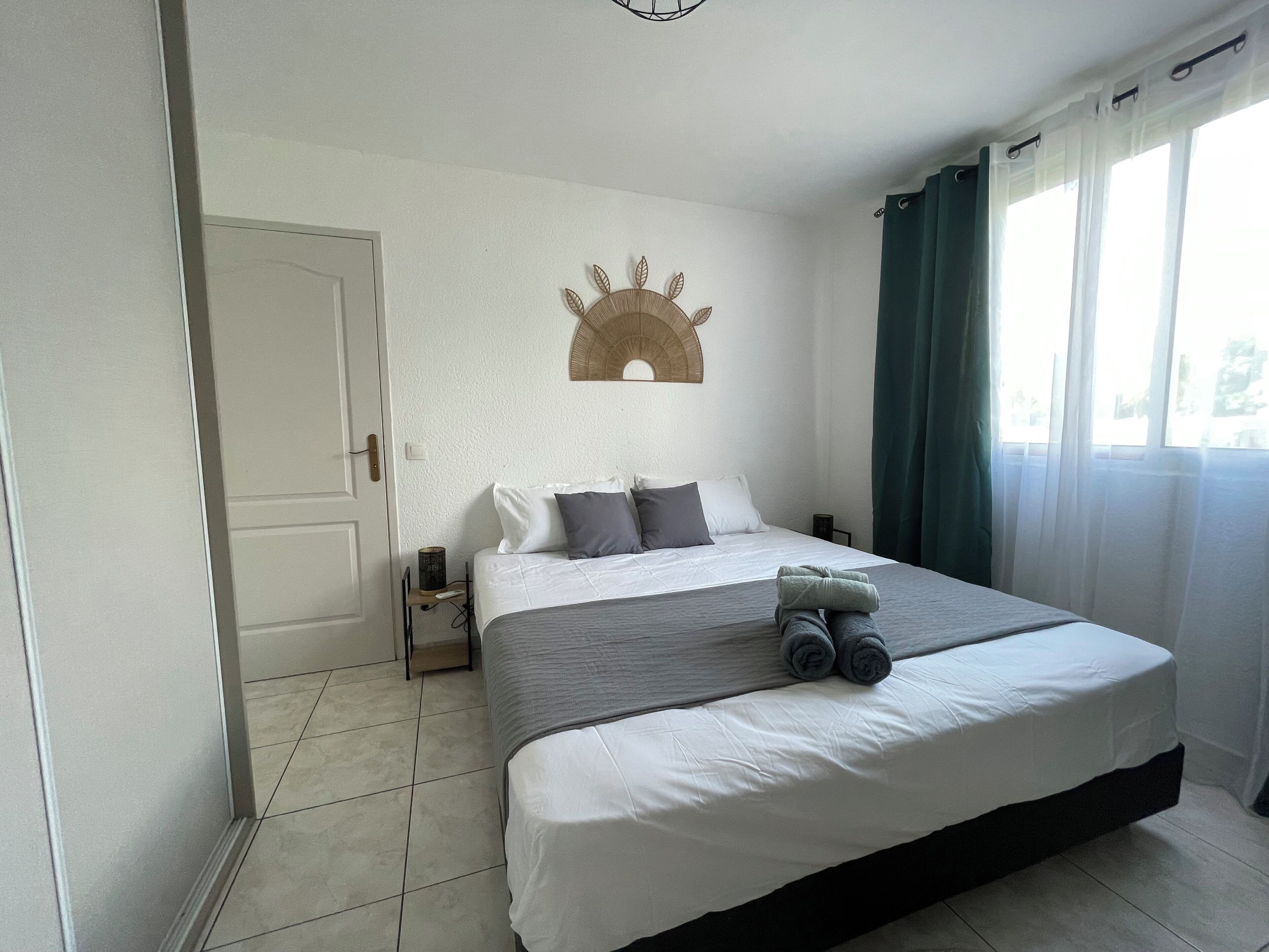 Een slaapkamer met een bed, een decoratief object aan de muur, een nachtkastje en een raam met gordijnen.