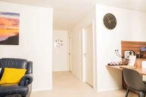 A modern living room with a black leather sofa, a yellow cushion, and a wall-mounted clock.