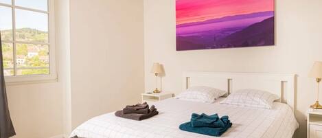 Un dormitorio con cama, mesita de noche, lámpara y un cuadro en la pared.