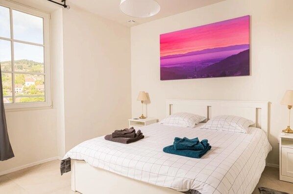 A bedroom with a bed, a nightstand, a lamp, and a painting on the wall.