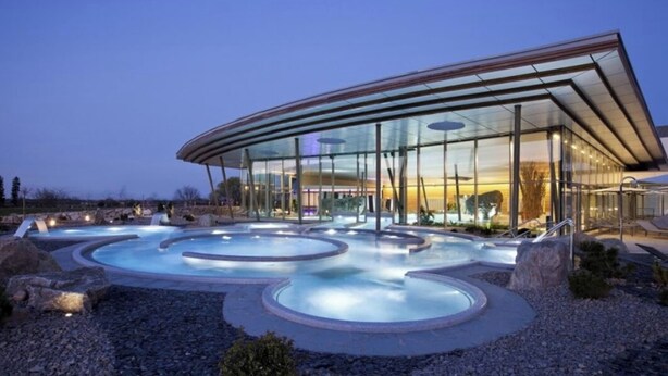 A modern building with a glass facade and a pool area with circular hot tubs.