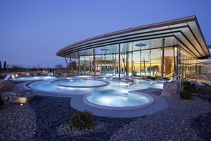 A modern building with a glass facade and a pool area with circular hot tubs.