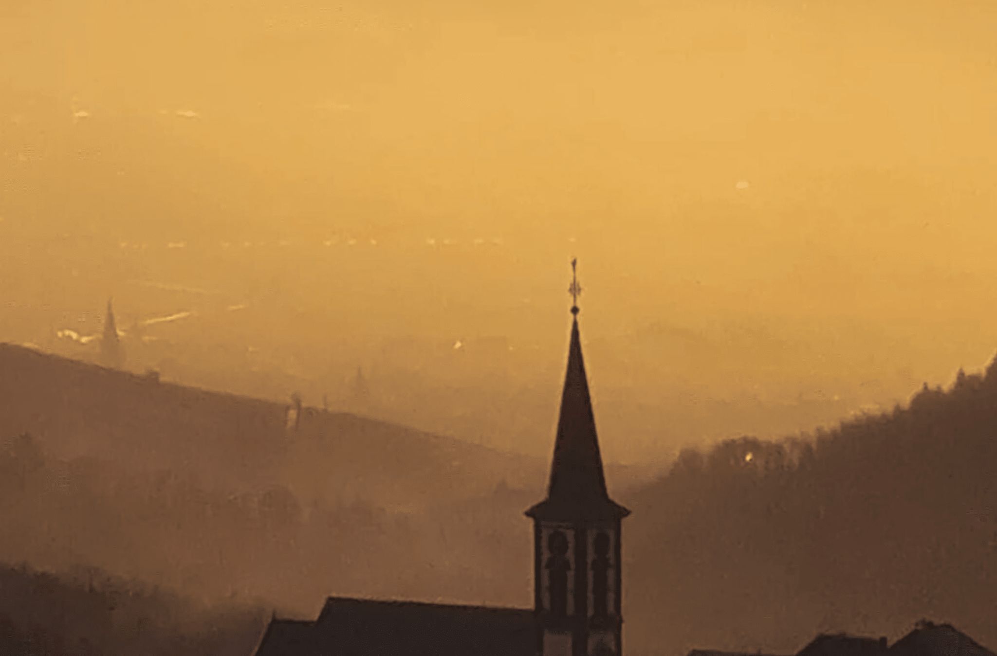 Eine Kirche mit einem markanten Kirchturm, eingebettet in eine hügelige Landschaft.