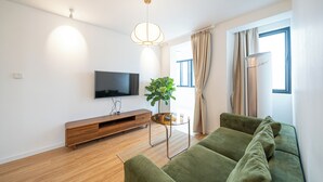 Un saló modern amb televisió de pantalla plana, moble de televisió de fusta, sofà verd i taula de centre de vidre.