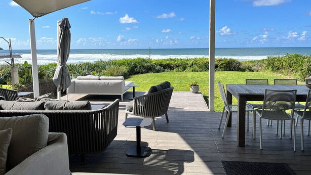 An outdoor patio with a view of the ocean, furnished with a sofa, chairs, and a table.