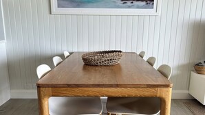 A dining table with a woven basket centerpiece, surrounded by white chairs with wooden legs, set on a wooden floor.