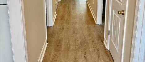 A hallway with wooden flooring, white doors, and a ceiling light fixture.
