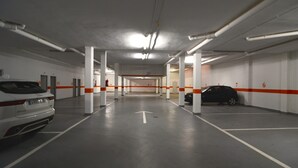 Un aparcamiento de varios niveles con paredes blancas, columnas rayadas en naranja y blanco, y un coche blanco estacionado en primer plano.