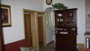 A living room with a red sofa, a wooden cabinet, a clock, and a door leading to another room. - Carrube House, in Andrano offers a terrace and sea views. (Marina di Andrano)