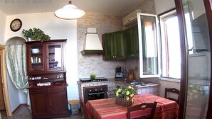 A kitchen with a dining table, chairs, a clock, cabinets, a stove, and a window. - Carrube House, in Andrano offers a terrace and sea views. (Marina di Andrano)