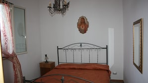 A bedroom with a metal bed frame, a bedside table with a lamp, a wall-mounted mirror, and a chandelier. - Carrube House, in Andrano offers a terrace and sea views. (Marina di Andrano)