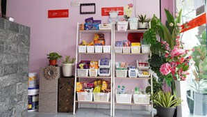 Ein Empfangsbereich mit einer rosa Wand, einem weißen Empfangsschalter und einer Pflanze. Schilder zeigen die Check-in- und Check-out-Zeiten an, und an der Wand befindet sich ein QR-Code.