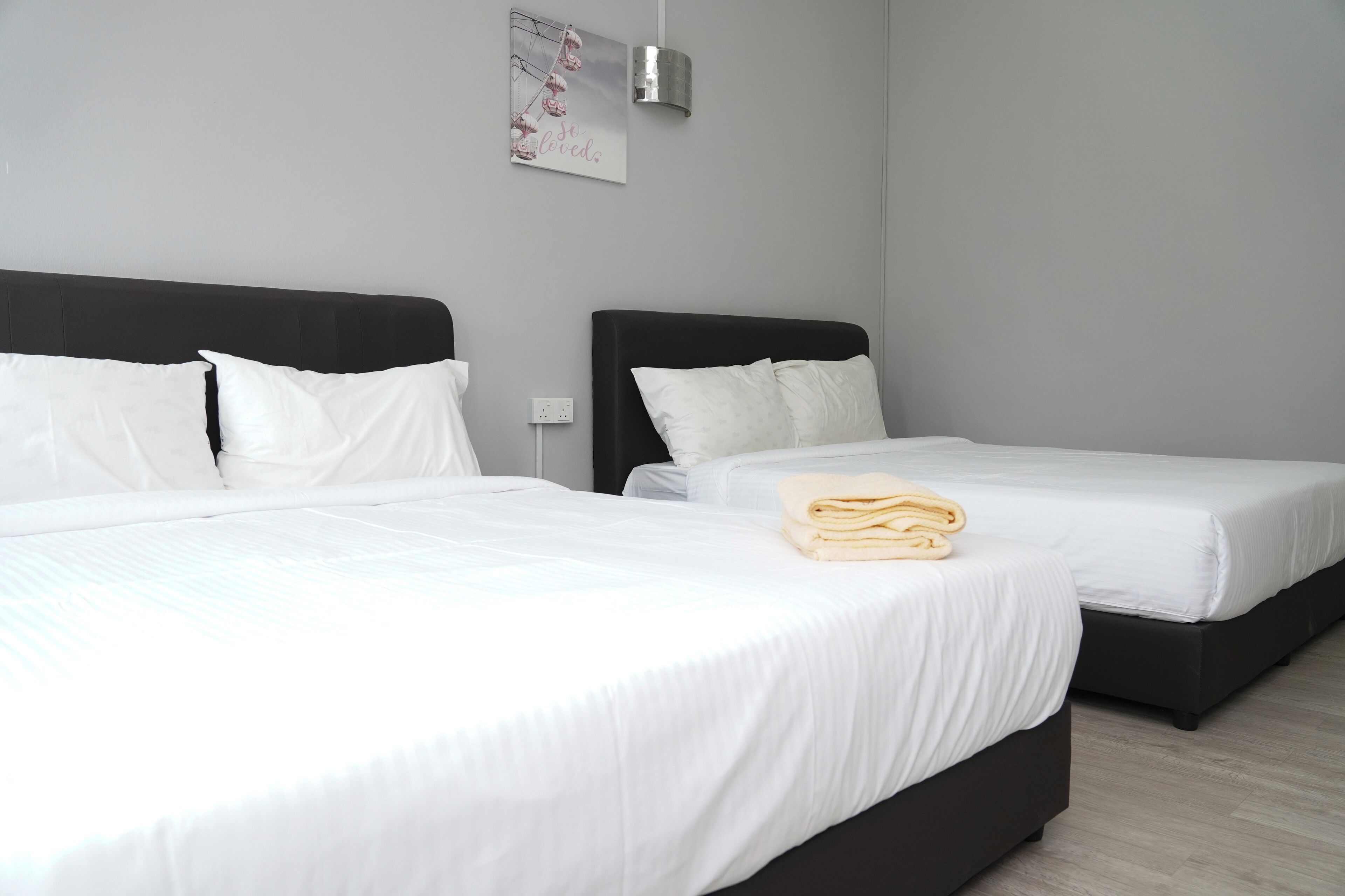 Habitación de hotel con dos camas, ropa de cama blanca, una lámpara de pared y un cartel.