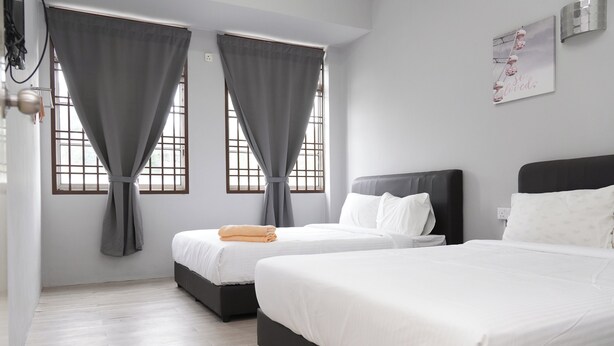 Ein Hotelzimmer mit zwei Betten, grauen Vorhängen, einer weißen Wand und einem Fenster mit Blick.