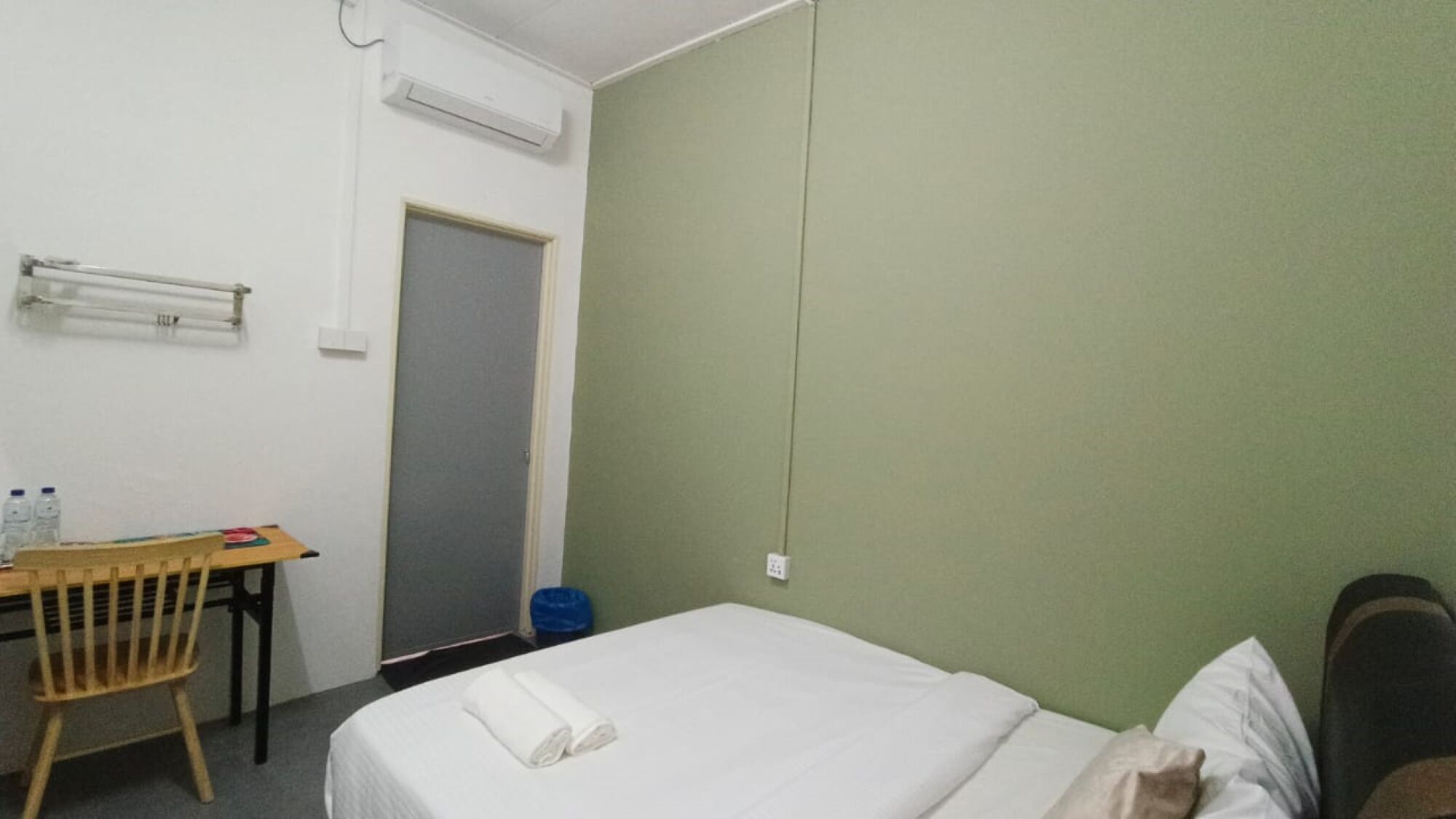A hotel room with a bed, a desk, a chair, and a door.