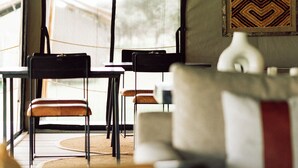 Un alloggio in tenda con zona pranzo, comprensivo di tavoli e sedie, e un divano con cuscino.