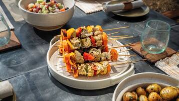 A table with skewers of grilled chicken and vegetables, a bowl of salad, and a bowl of roasted potatoes.