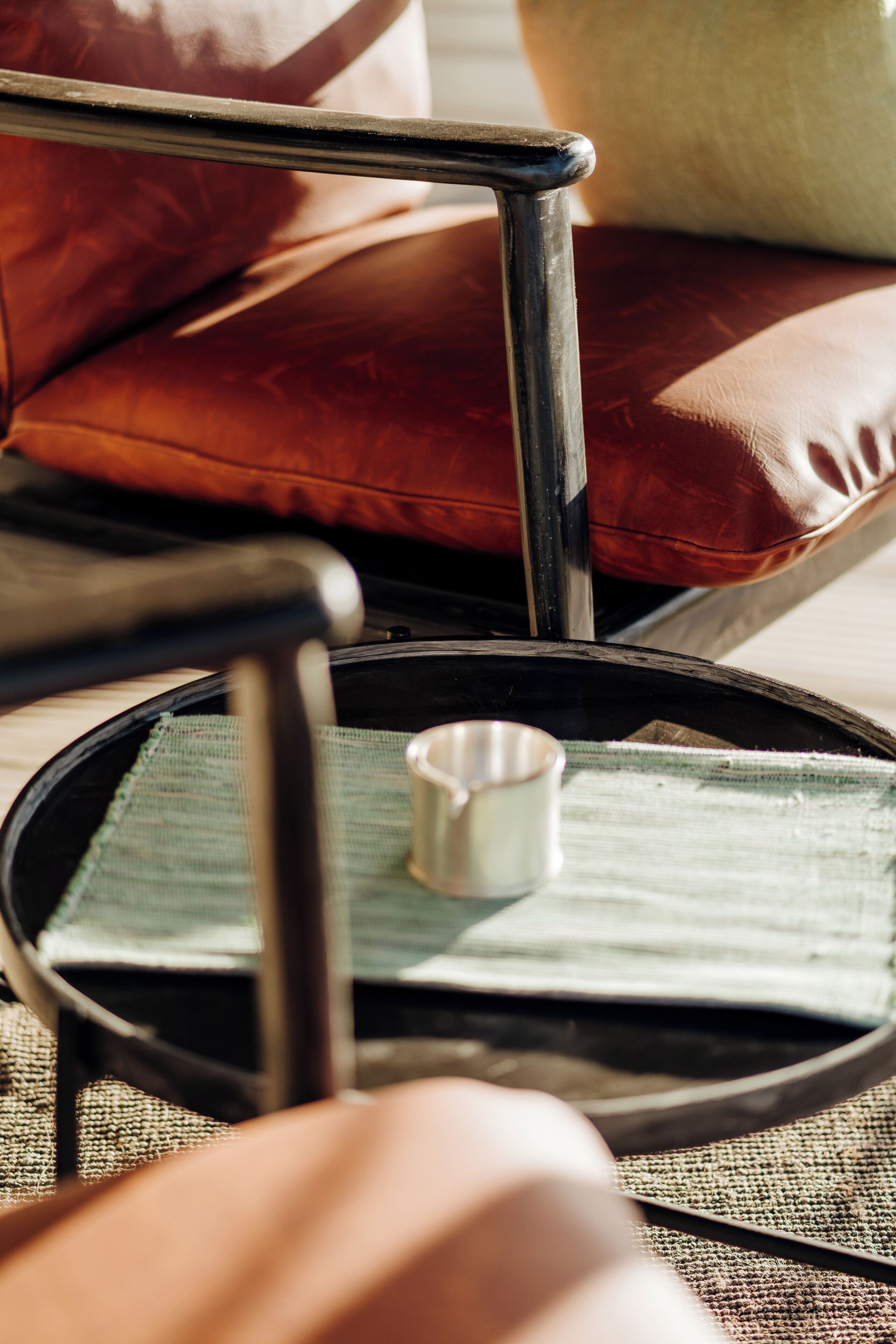 A chair with a metal frame and a cushion, a tray with a metal cup, and a woven mat on a wooden floor.