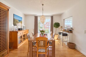 A spacious dining area with a wooden table and chairs, a chandelier, and a view of the city through large windows.