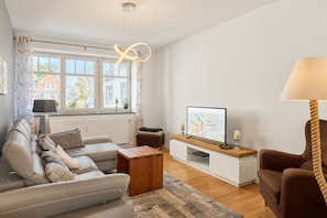 Una sala moderna con sofá, una mesa de centro, un televisor sobre un soporte de madera y una lámpara.