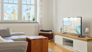 A modern living room with a large window, a flat-screen TV, a wooden coffee table, and a white sofa.