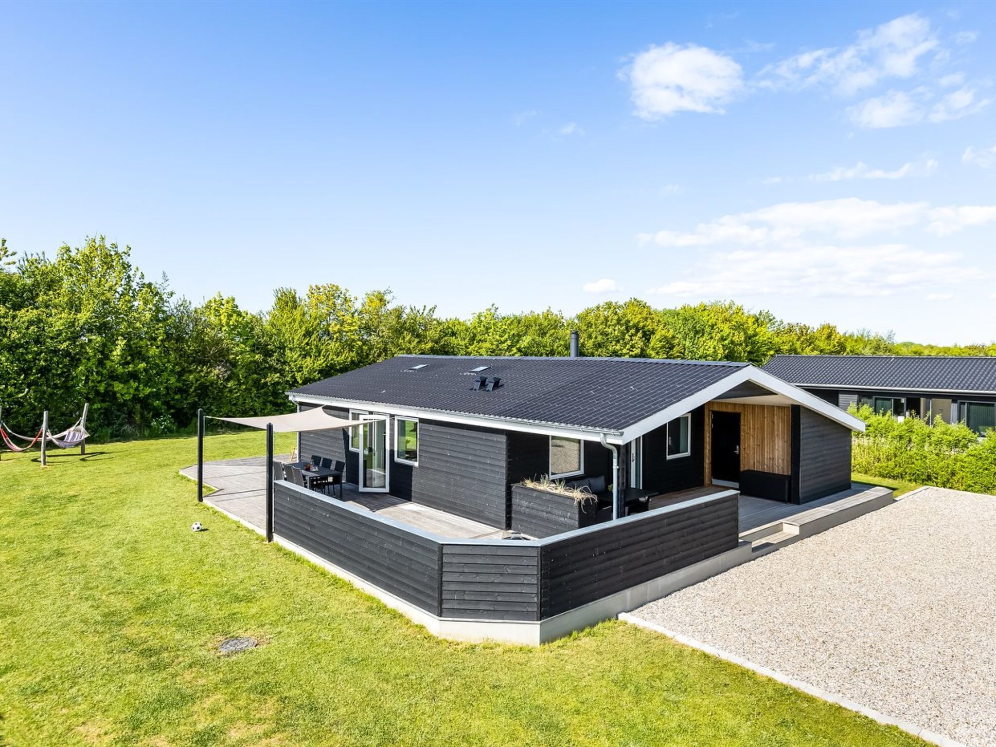 A modern house with a large deck, a covered patio, and a gravel driveway.