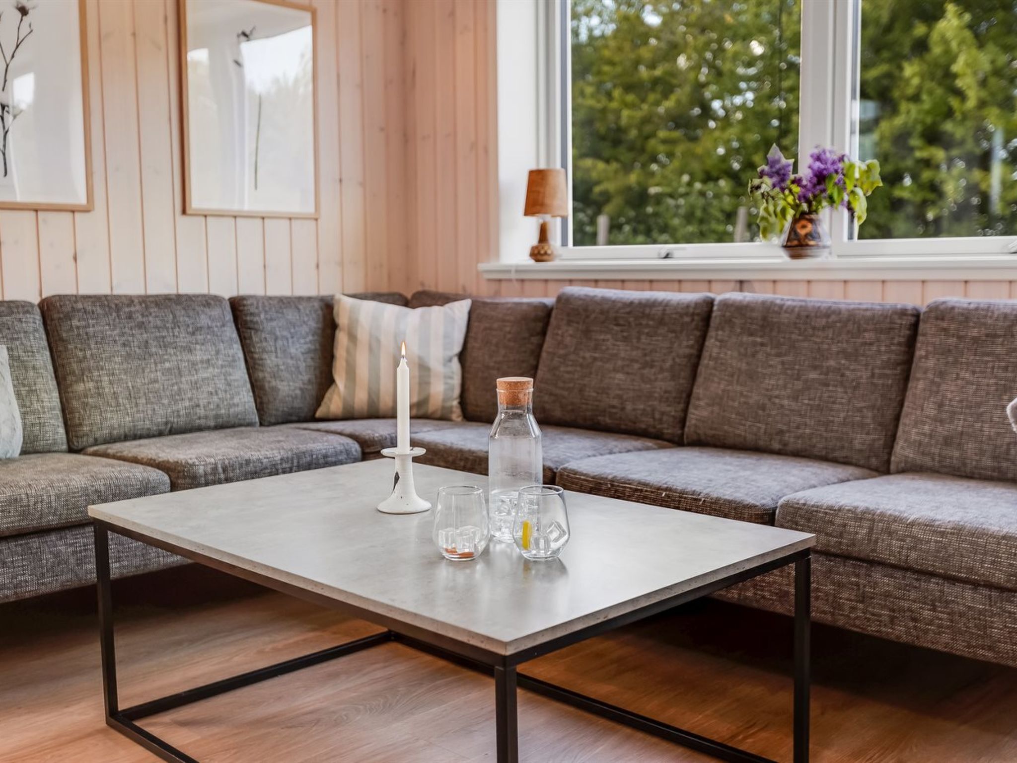 Un salon moderne avec un canapé d’angle gris, une table basse en bois et une fenêtre donnant sur des arbres.