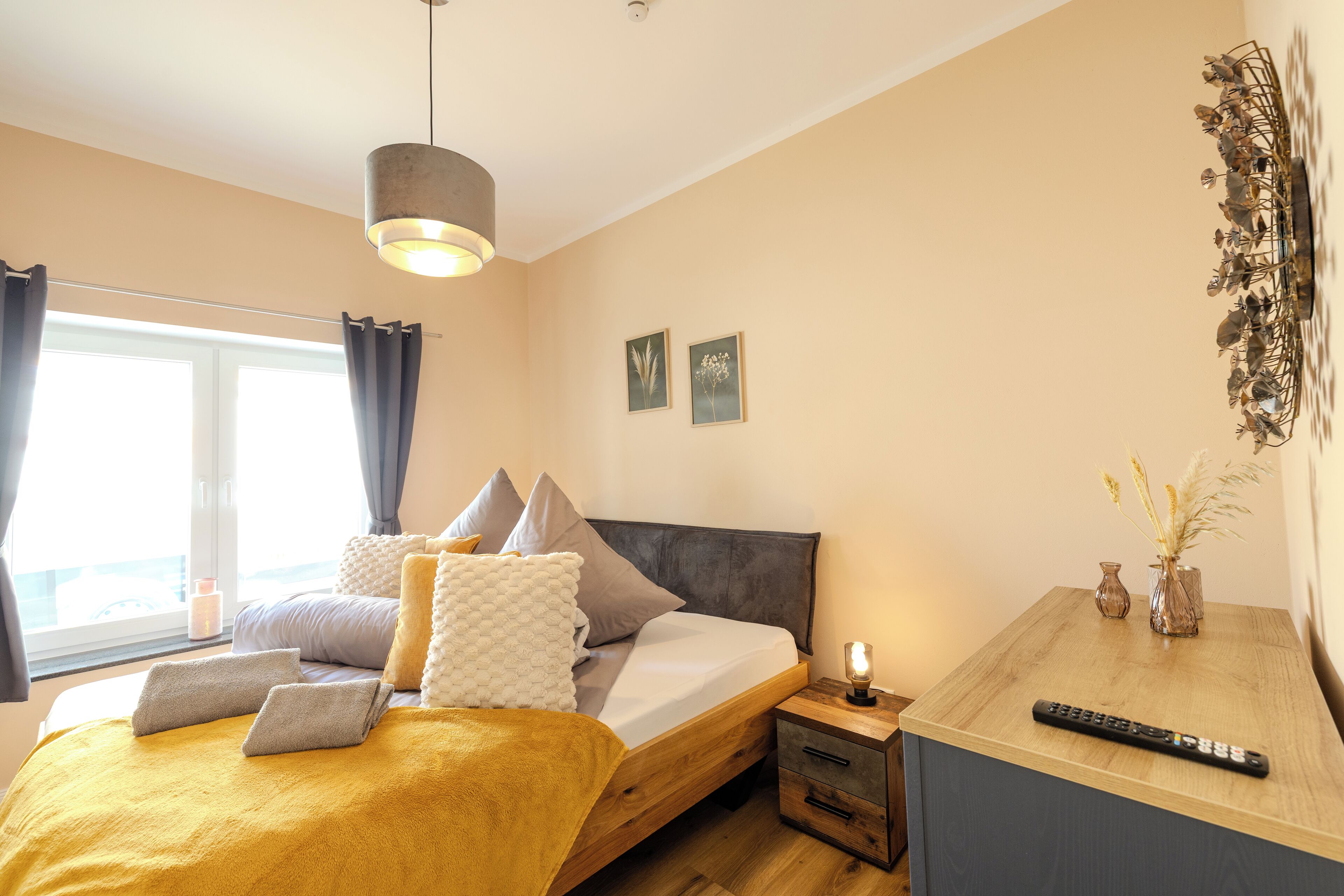 A bedroom with a bed, bedside table, lamp, and a view of the outside.