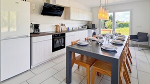 A modern kitchen with a dining area, featuring a large table set for six, a built-in oven, and a flat-screen TV above the counter. - La Maison Bleue, on the Bay of the Somme, in a peaceful natural setting (Pendé)